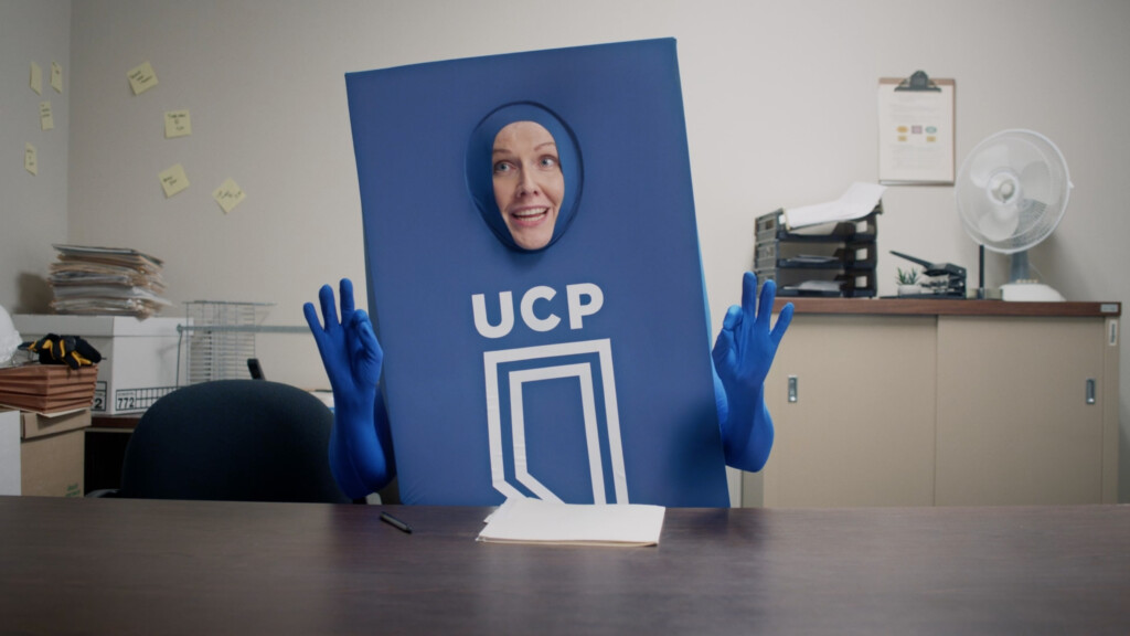 A blue person wearing in a costume shaped like Alberta says UCP on it.